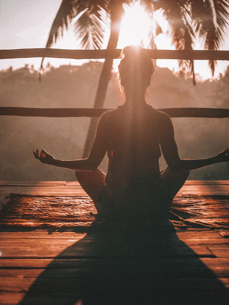 Persona meditando sentada al amanecer sobre una terraza de madera